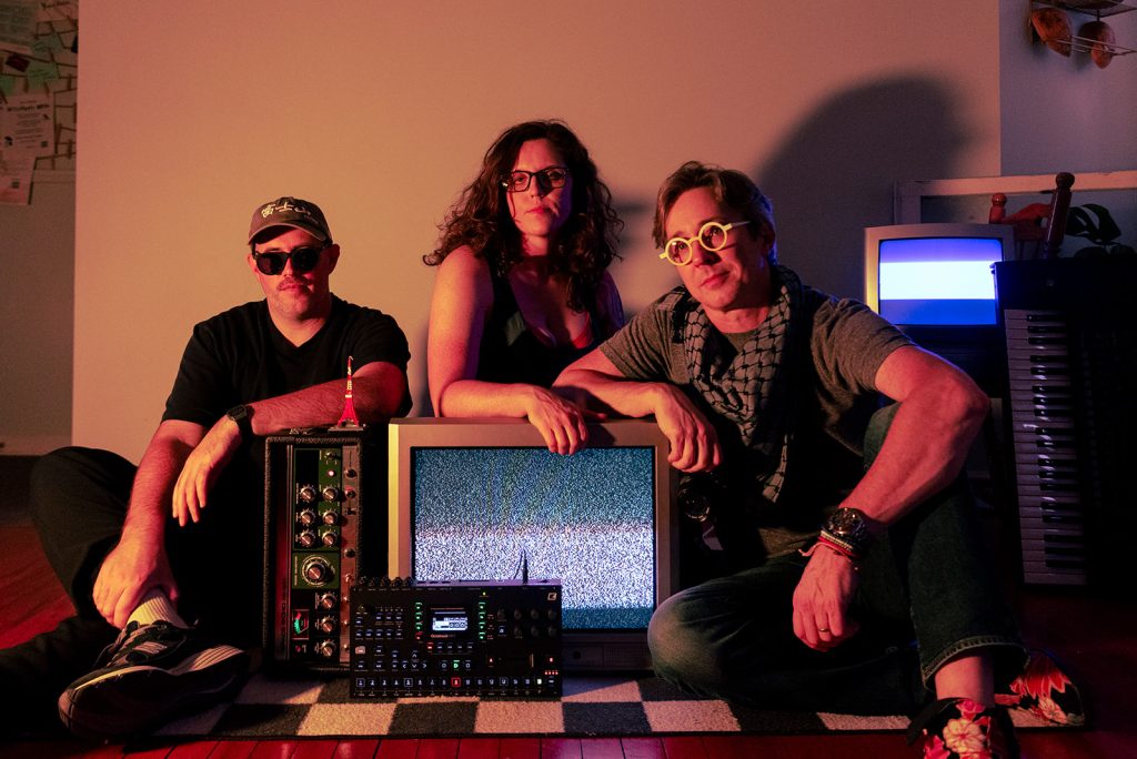 Joe, Perry, and Justin sit amongst their music gear and vintage televisions